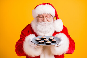 Close-up portrait of his he nice cheery hungry white-haired Santa holding in hands smelling domestic fresh tasty yummy sushi roll tuna maki isolated bright vivid shine vibrant yellow color background