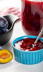 Homemade damson plum jam in blue ceramic bowl and berries on white wooden background.