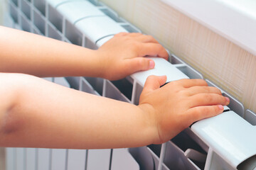 Child getting warmer up her hands over an electric radiator of heating at home.Problems with home heating