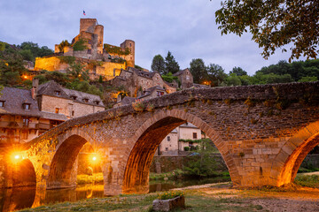 Medieval French Belcastel village with stone arched bridge across Aveyron river and ancient castle on hill in sumer twilight
