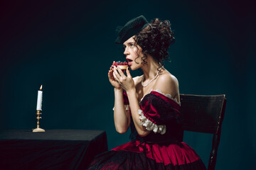 Forbidden sweets. Young woman as Anna Karenina isolated on dark blue background. Retro style, comparison of eras concept. Beautiful female model like literature character, great, old-fashioned.