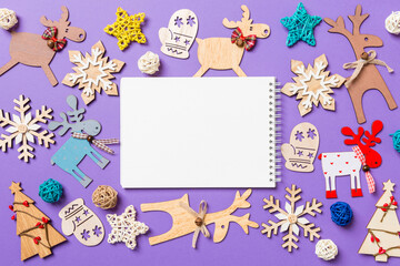 Festive decorations and toys on purple background. Top view of notebook. Merry Christmas concept