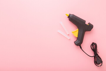 Black glue gun with plastic sticks on light pink background. Pastel color. Closeup. Empty place for text. Top down view.