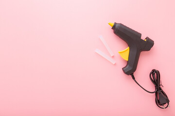 Black glue gun with plastic sticks on light pink background. Pastel color. Closeup. Empty place for text. Top down view. - obrazy, fototapety, plakaty