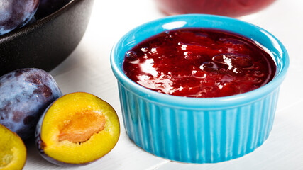 Homemade damson plum jam in blue ceramic bowl and berries on white wooden background.