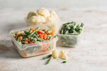 Frozen vegetables: a mix of vegetables, string beans and cauliflower in various plastic containers for freezing on a light background.