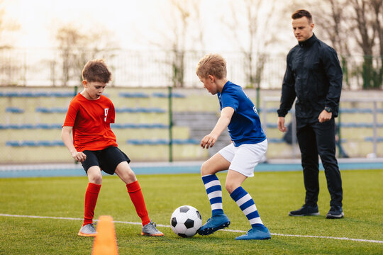 Young boys on soccer practice training with coach. Junior footballers compete on training unit. Young coach coaching sports school kids. School soccer stadium in blurred background