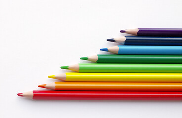 multicolored pencils, rainbow colors, lie horizontally, on a light, white background. Steps, stairs made of colored pencils. Subjects for creativity, art school,