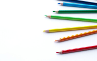 multicolored pencils, rainbow colors, lie chaotically horizontally, to the right, on a light, white background. Scattered multicolored pencils on the right. Subjects for creativity, art school,