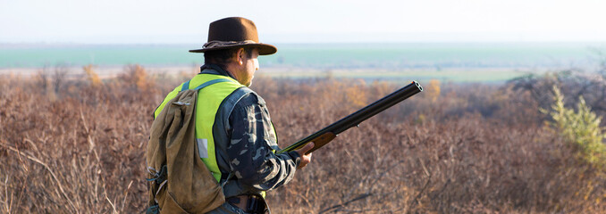 Hunter man in rural field with shotgun and backpack during hunting season