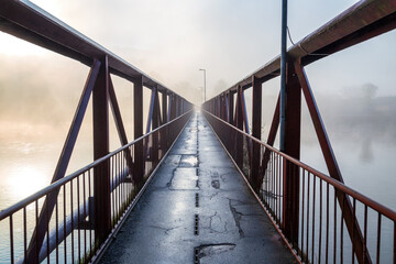 Iron bridge for pedestrians over the river in a misty morning.