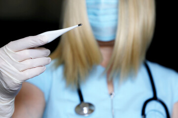 Coronavirus symptoms, woman in medical mask measures body temperature. Doctor with digital...