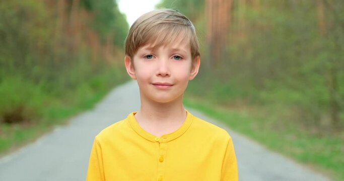 Closeup face of  little boy looking to camera on the nature.  White boy of 8 years old is staring, outdoors. Slowly zooming  to the child's face.
