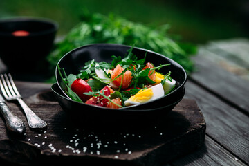 Salad with salmon, arugula and egg in a black plate 