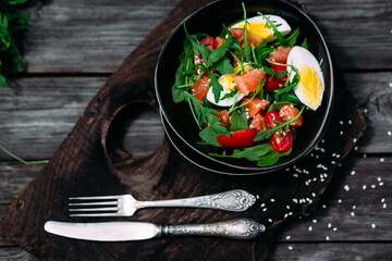 Salad with salmon, arugula and egg in a black plate 
