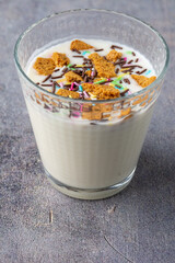 Top closeup of a glass with natural yogurt, biscuit pieces and colors, on gray background, in vertical