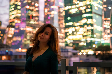 A young woman stands at night in front of glowing glass skyscrapers in Moscow. High ISO, grainy and noisy images.