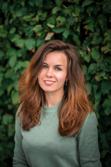 Portrait of a young brunette woman with long hair on a background of green leaves