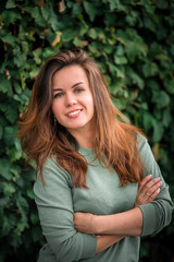 Portrait of a young brunette woman with long hair on a background of green leaves