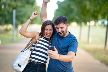 Happy couple celebrating that they have won an award on their smartphone in the park