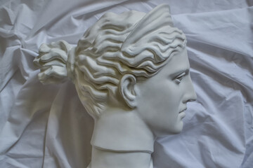 Ancient greek statue white plaster marble head of diana on a background of white fabric drapery with folds