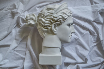 Ancient greek sculpture white plaster head of diana on a background of white fabric drapery with folds