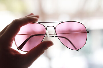 gafas de sol  color rosa sujetadas por un lado con un fondo de ciudad fuera de foco