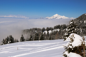 Snowy paradise high in the mountains with the view over alps and thick fog in the valley below