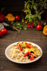 Porridge couscous with baked vegetables, zucchini and onions, bell peppers and eggplants with spices, plate with food on a dark wooden background