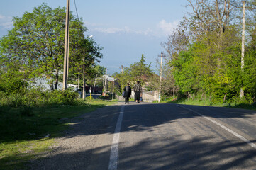 Fototapeta na wymiar Two Women Walking down a Road in a Small Georgian Village near Sighnaghi with view onto the Caucasus Mountains, Georgia
