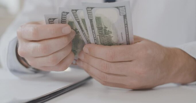 Close-up of male Caucasian hands counting dollars. Unrecognizable man in physician uniform holding pack of money. Bribery in medicine. Doctor calculating salary. Cinema 4k ProRes HQ.