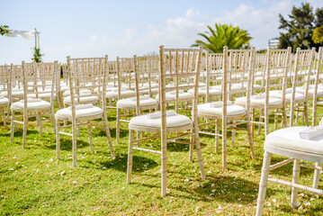 Fototapeta na wymiar Closeup on wedding decorated empty wooden chairs for guests on green grass. Sunny day time outdoors background.