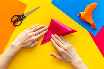 Female hands folding sheet of paper - origami bird. Overhead view