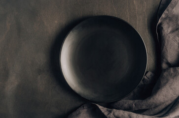 Black table setting: plates, napkin, silverware on black wooden background