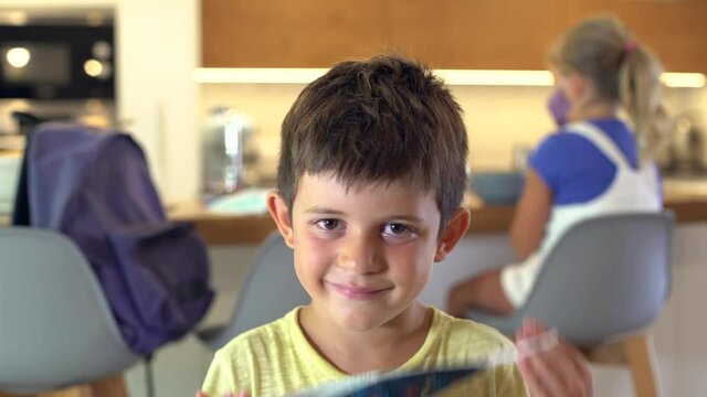 Caucasian kid puts on a protective mask at home looking at camera on First day School at the kitchen at home. Concept new rules, new normality during Coronavirus, COVID-19.
