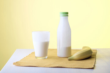 on the table, covered with a napkin, are a banana and a bottle with a glass of milk
