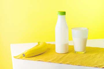 on the edge of the table there is a bottle and a glass with a dairy product next to a banana, the background is yellow