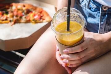Close-up of hands holding a plastic glass with smoothies on a pizza background. Street food concept