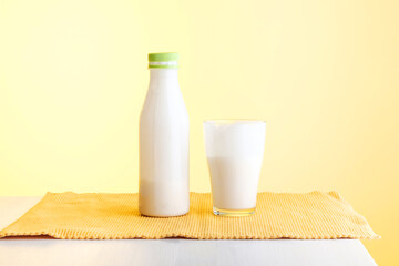 a bottle with a dairy product and a glass filled with yogurt on the table, the background is yellow