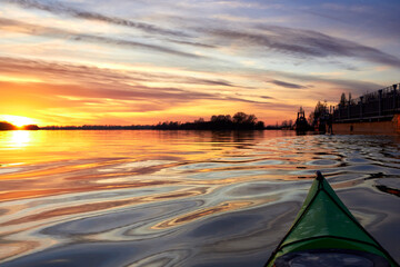 View from bow (prow) of green kayak at colorful sunset over Danube river at autumn time