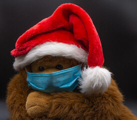 Un mono marrón de peluche con mascarilla y gorro de Papa Noel rojo