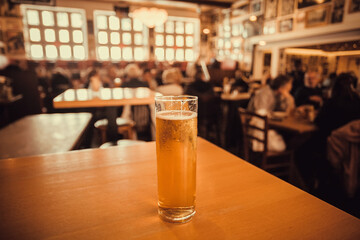 One beer glass on table of busy bar, with crowd of people. Interior of pub with fresh lager beer inside. Brewery and leisure