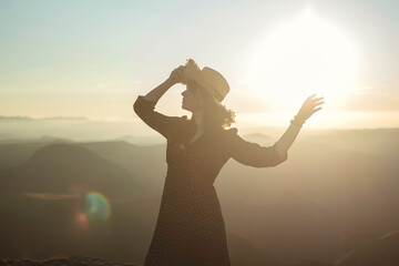 silhouette of a woman with arms outstretched in sunset light in mountains