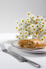 Strudel in a plate on a white plate with daisies and cutlery.