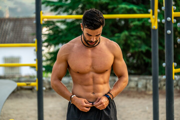 Close portrait of young Latin man without a shirt and black pants and mask training on the bar of a calisthenics park