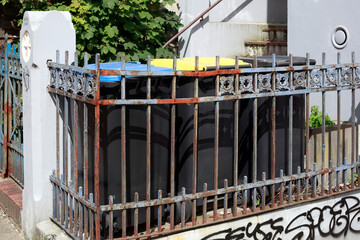 Bunte verschiedene Wertstofftonnen, vor einem wohnhauss hinter einem alten Gartenzaun stehend, Deutschland