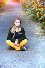 Young woman in lotus position sitting on the green path in the autumn park. Calm and meditation concept.