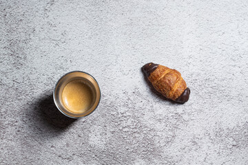 Espresso coffee and tiny chocolate croissant isolated on a rough grey background