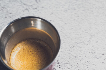 Espresso creamy coffee served on a metal circle cup on a rough white background board