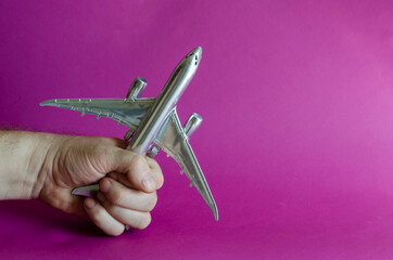 A hand holds a model of a silver airplane.
